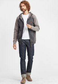 Sweatshirt jacket with a grey fleece body, contrasting grey sleeves, front zipper, two pockets, and textured drawstrings. Worn over a white shirt.