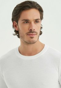 Pull en tricot blanc avec un col rond. Présente un tissu texturé et une silhouette ajustée, mettant en valeur un design décontracté et épuré.