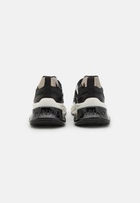 Sneaker bianco e nero con una parte superiore texturizzata, colletto imbottito, dettagli lucidi sul tallone e il marchio "PINKO" sul tallone.