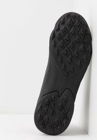 Musta urheilu kengän pohja, jossa on tekstuuri pinta, ja timanttimainen kuvio sekä reliefillä varustettu logo. Kaarevat reunat ja tasaiset alueet ovat läsnä.