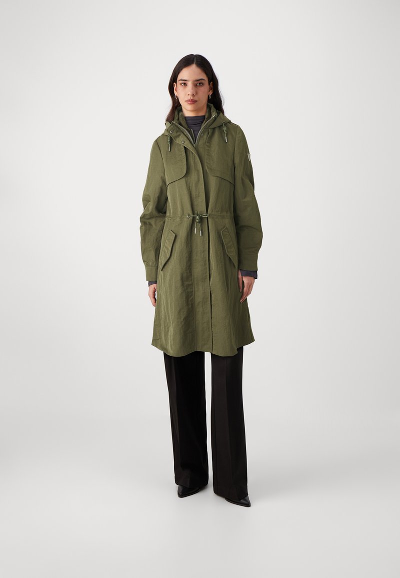 Parka verde oliva con cappuccio, vita aderente, due ampie tasche frontali e vestibilità comoda. Tessuto testurizzato con finitura opaca.