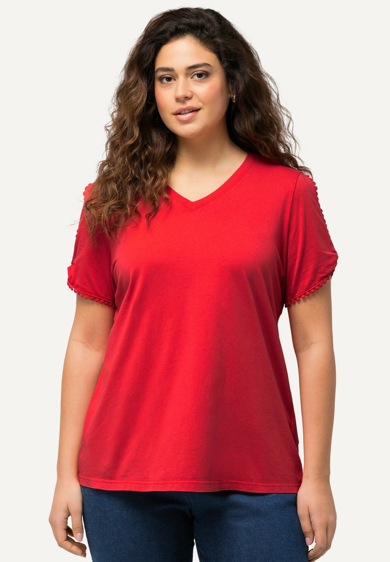 Camiseta de algodón roja con cuello en V, mangas cortas con detalles de crochet, corte relajado y textura suave, combinada con pantalones de mezclilla azules.