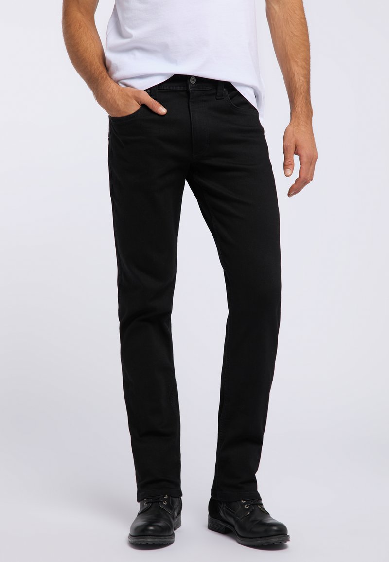 Czarne dżinsy o slim fit, wykonane z denimu. Posiadają pięć kieszeni i zapięcie na guzik, zestawione z czarnymi butami. Prosty design.