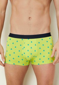 Männer-Boxershorts aus leuchtend gelbem Baumwollstoff mit einem marineblauen Bund, der mit einem Muster aus kleinen blauen Äpfeln im gesamten Stoff versehen ist.