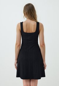 Abito nero con un motivo zigzag texturizzato, design senza maniche, schiena quadrata e gonna svasata che arriva sopra il ginocchio.