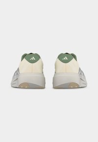 Ζευγάρι αθλητικών παπουτσιών σε εκρού και πράσινο, που φαίνονται από πίσω, με παχιά λευκή σόλα και το λογότυπο της Adidas στις ταμπέλες της φτέρνας.
