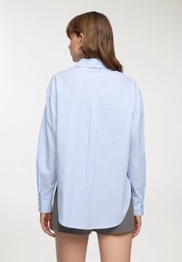 Camicia a strisce blu chiaro con vestibilità rilassata, maniche lunghe, piega sul retro e orlo arrotondato, realizzata in tessuto intrecciato.