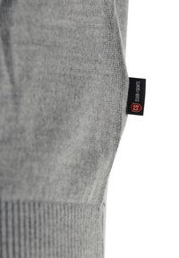 Grau gestricktes Kleidungsstück mit glatter Textur. Verfügt über ein schwarz-rotes Etikett mit der Aufschrift "CLUB 8 GENTS" an der Seitennaht. Einfaches und modernes Design.