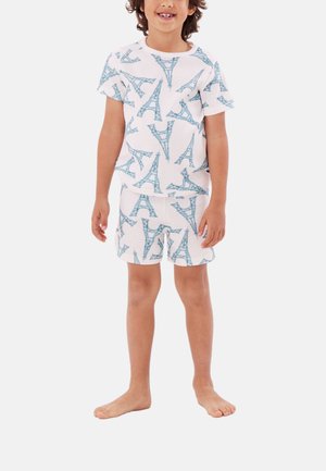 Kind trägt weißes Kurzarmshirt und Shorts mit blauem Eiffelturm-Muster, steht barfuß vor einem schlichten Hintergrund.