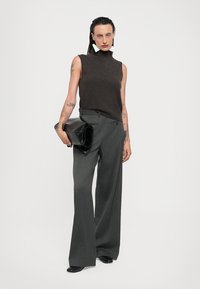 Brown sleeveless turtleneck sweater, gray high-waisted wide-leg trousers, and a black oversized clutch. Smooth textures, minimal design.