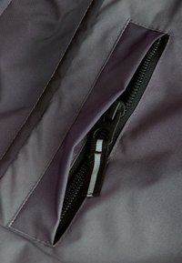 Tissu imperméable gris avec une fermeture éclair noire visible et une poche. La fermeture éclair a des dents noires et une languette en tissu avec des accents blancs.