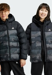 Des vestes matelassées noires et grises avec capuches, arborant un design camouflage et des fermetures éclair à l'avant. Le logo adidas est visible en haut à gauche.
