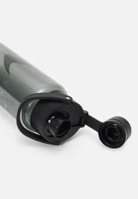 Transparante grijze plastic waterfles met een zwarte schroefdop en een handvat in de lus, met een brede opening en een draagriem.