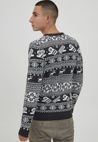 Schwarz-weißer Strickpullover mit einem Wintermuster, das Rentiere, Schneeflocken und geometrische Formen zeigt. Rippbündchen und Saum.
