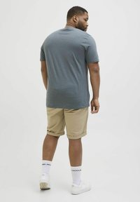 T-shirt gris à manches courtes, en tissu coton, coupe décontractée, associé à un short beige retroussé, des baskets blanches et des chaussettes blanches avec logo.