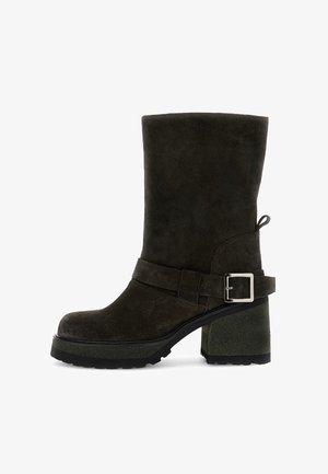 Stivaletto in suede verde scuro con tacco ampio e rettangolare. Presenta una cinghia con una fibbia argentata e una suola texturizzata.