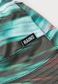 Fargerik, bølgende mønster med teal og svarte nyanser på en vanntett lue. Inkluderer en fremtredende "RAINS"-etikett sydd på siden.