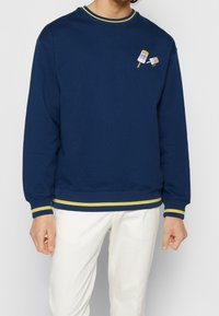 Sweatshirt bleu marine en coton doux, avec un col rond et des accents rayés jaunes au niveau du col et de l'ourlet. Comprend une broderie ludique de glace.