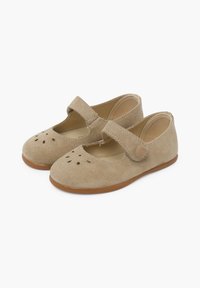 Beżowe zamszowe buty typu Mary Jane z okrągłym noskiem, okrągłymi detalami wycięć, zapięciem na rzep i płaską gumową podeszwą.