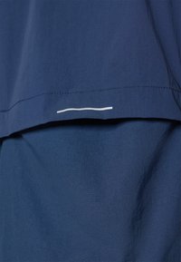 Mørkeblåt stof med lagdelt design og en glat tekstur, der har en hvid vandret linje som accent langs den nederste kant.