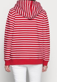 Hoodie a righe rosse e bianche con orlo curvato, maniche lunghe e una texture morbida. Presenta un cappuccio con cordino e polsini a coste.