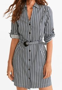 Abito camicia al ginocchio a righe verticali blu e bianche. Presenta una chiusura con bottoni sul davanti, maniche arrotolate e una cintura di tessuto in vita.