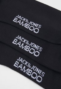 Schwarze Bambussocken mit weißem Text "JACK & JONES BAMBOO", der in einer klaren, fetten Schrift über den Stoff gestrickt ist.