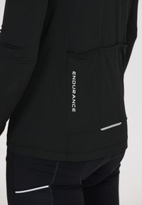 Close-up of a person wearing black athletic clothing with "ENDURANCE" text on the back pocket area and reflective strips on jacket and pants.