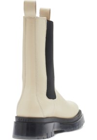 Bottine en cuir beige avec des panneaux élastiques noirs sur les côtés, semelle en caoutchouc noir plate, design structuré et languettes pour un enfilage facile.