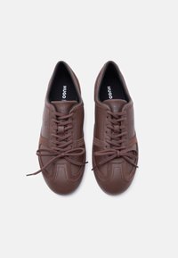 Ζευγάρι καφέ δερμάτινα αθλητικά παπούτσια Hugo με κορδόνια δεμένα σε φιόγκους, φωτογραφημένα από πάνω σε λευκό φόντο.