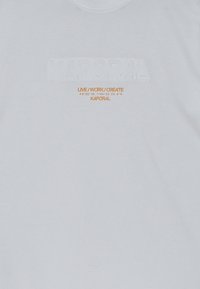 Witte katoenen T-shirt met reliëf "KAPORAL" logo en oranje tekst met de tekst "LIVE / WORK / CREATE" en geografische coördinaten.