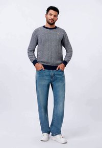 Μπλε ναυτικό και λευκό πλεκτό πουλόβερ με σχέδιο ψαροκόκκαλο, με ραβδωτά μανσέτες και τελείωμα. Ανοιχτό γαλάζιο τζιν με ευθεία γραμμή και λευκά αθλητικά παπούτσια ολοκληρώνουν το ντύσιμο.