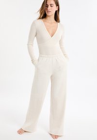 Beżowa prążkowana bluzka z dzianiny z długim rękawem i głębokim dekoltem w serek, zestawiona z beżowymi, luźnymi spodniami do domu z elastycznym pasem.