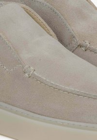 Jasno beżowe zamszowe buty typu slip-on z gładką fakturą, kontrastowym przeszyciem i okrągłym czubkiem oraz białą gumową podeszwą.
