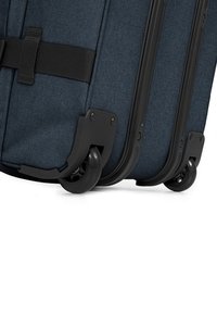Valigia blu con superficie in tessuto testurizzato, accessori neri e tre ruote scorrevoli; presenta una cinghia di compressione per una chiusura sicura.