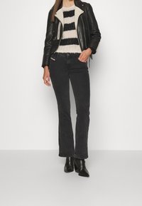 Jeans negros de campana combinados con una chaqueta de cuero negra con un collar crema y un suéter de punto a rayas blancas y negras. Botines negros.