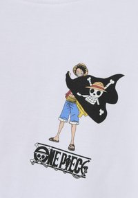 T-shirt blanc avec un graphique d'un personnage portant une cape noire ornée d'une tête de mort et de tibias croisés, et le texte "ONE PIECE" en dessous.
