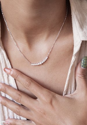 Silberne Halskette mit geschwungenem Design und mehreren klaren Steinen. Die Kette ist zart und liegt auf dem Schlüsselbein des Trägers.