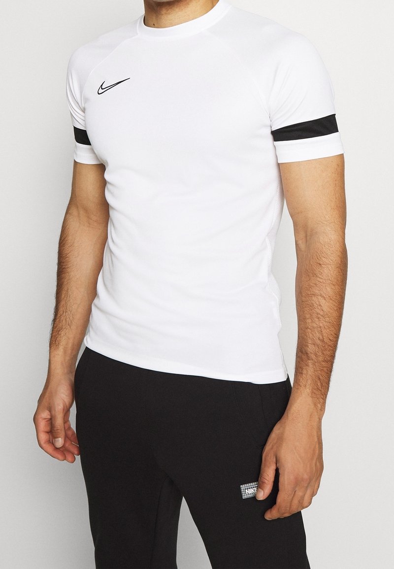 Valkoinen urheilupaita lyhyillä raglan-hihoilla, jossa on mustat yksityiskohdat hihansuissa ja pieni musta Nike-logo rinnassa.