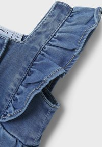 Denim kleita ar ruflētiem plecu akcentiem, gaiši zila krāsa, redzams vīlējums un v-veida dekoltē. Iekļaujuz etiķeti, kas norāda izmēru 1-2 gadi.