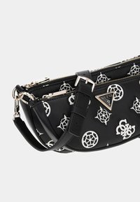 Musta keinonahkainen olkalaukku valkoisilla kuvioilla, kaksinkertaiset vetoketjulliset taskut, säädettävä hihna ja metallinen logoelementti.