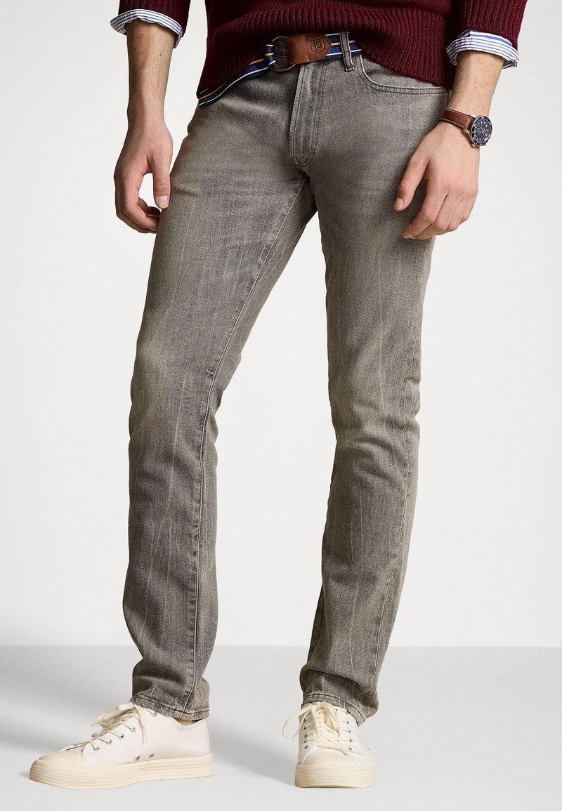 Slim-fit grå denim jeans med en blekt finish, kombinerade med vita sneakers och ett brunt läderbälte i midjan, med subtil textur och sömmar.