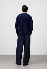 Maglione blu navy con un motivo testurizzato e maniche lunghe, abbinato a pantaloni larghi blu navy. Tessuto morbido e vestibilità rilassata. Design minimalista.