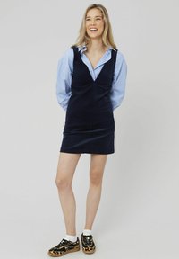Robe en velours côtelé bleu marine avec un design en V, associée à une chemise à rayures bleues et des baskets imprimées léopard. Présente une silhouette ajustée.