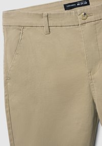 Beżowe spodnie bawełniane z klasycznym wzornictwem, z zamek błyskawicznym, kieszeniami z przodu i z tyłu oraz pojedynczym zapięciem na guzik. Etykieta zawiera dane dotyczące rozmiaru.