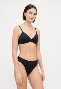 Schwarzes Bikini-Set mit einem dreieckigen Bralette, dünnen verstellbaren Trägern und tief sitzenden Slips. Das Material sieht glatt und dehnbar aus.