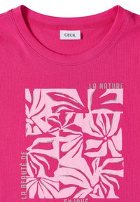 Camiseta de color rosa brillante con escote redondo, estampado floral en bloques y texto plateado que dice "La Nature" y "La Beauté De".