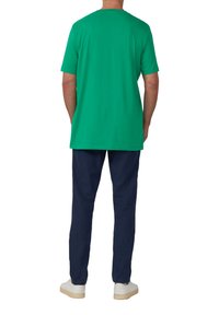 Zielona bawełniana koszulka z krótkimi rękawami i okrągłym dekoltem, zestawiona z granatowymi spodniami i białymi trampkami, widok od tyłu.