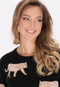 Černý svetr s texturovaným pletením a béžovými tygřími motivy. Modelka má dlouhé vlnité vlasy a nosí zlaté naušnice.