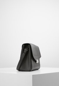 Borsa nera in pelle con una forma strutturata, caratterizzata da una pattina frontale, tracolla regolabile e un accento metallico argento sulla chiusura.